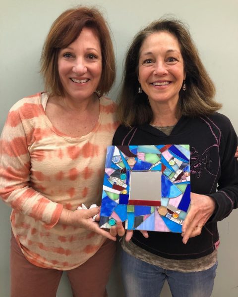 2 women smiling at the camera holding a piece of glass work