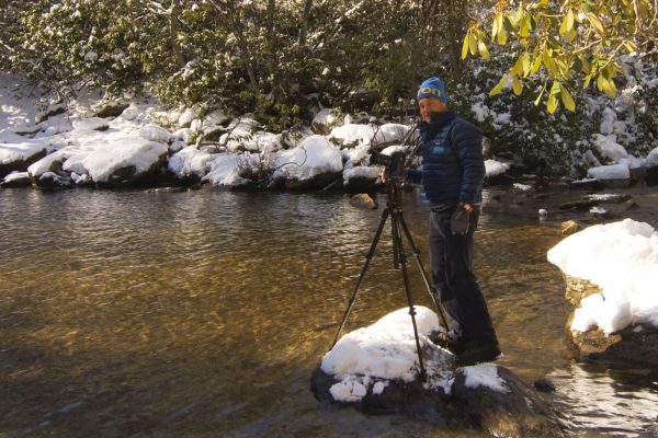 Camera man smiling while standing on a stone in a river
