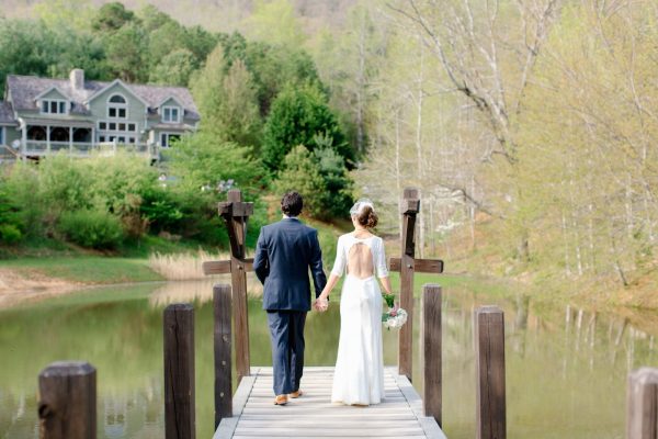 Bride and Groom walking away from the camera down a dock on a small lake