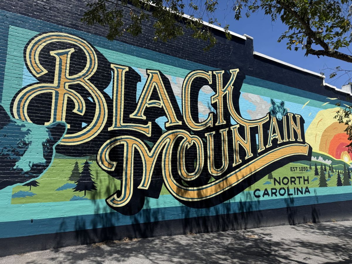Colorful "Black Mountain, North Carolina" mural painted on a downtown brick building, featuring stylized mountain landscapes, evergreen trees, a sunrise, and bold vintage lettering that celebrates the town's mountain heritage.