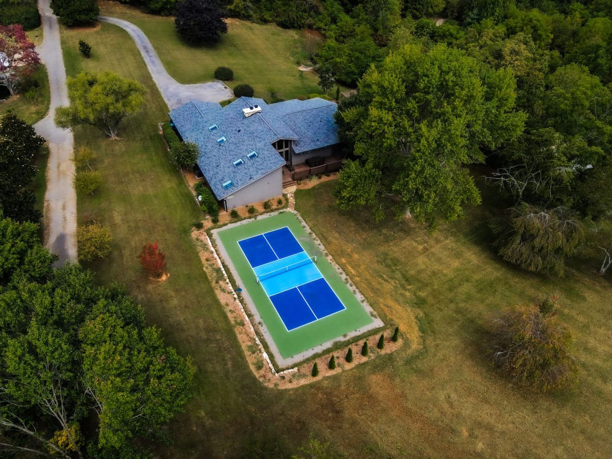 Bird's-eye view of a pickleball court next to a house and surrounded by trees