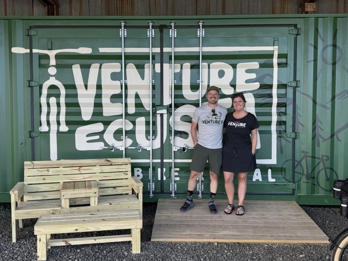 The owners of Venture Ecusta Bike Rental standing in front of their green branded container at the Ecusta Trail trailhead in Hendersonville, NC.