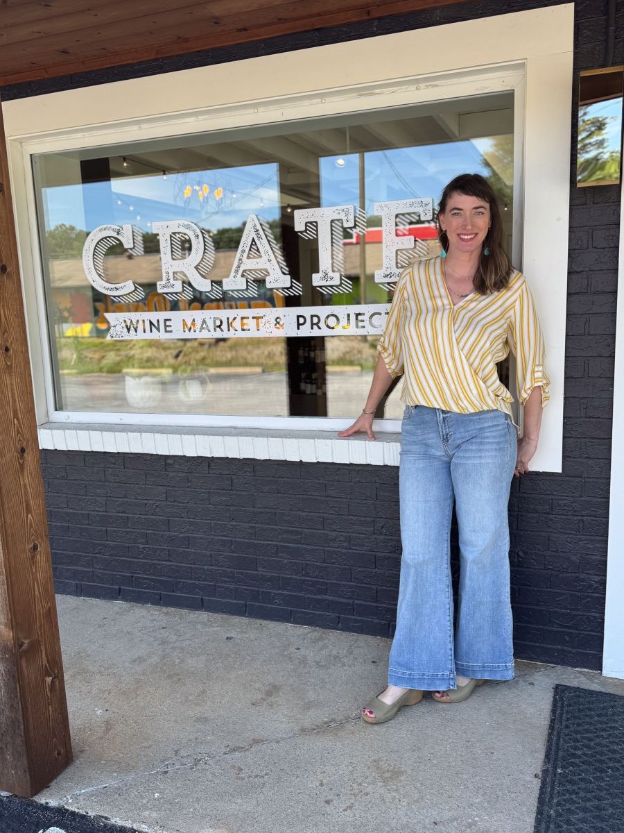 A woman standing outside Crate Wine Market & Project in Hendersonville, NC, smiling beside the shop’s front window.