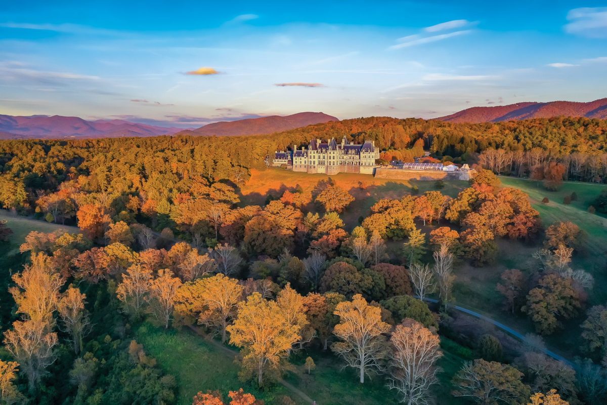 Aerial view of Biltmore Estate in Asheville, North Carolina during fall, with vibrant autumn foliage surrounding the historic mansion and Blue Ridge Mountains in the background.