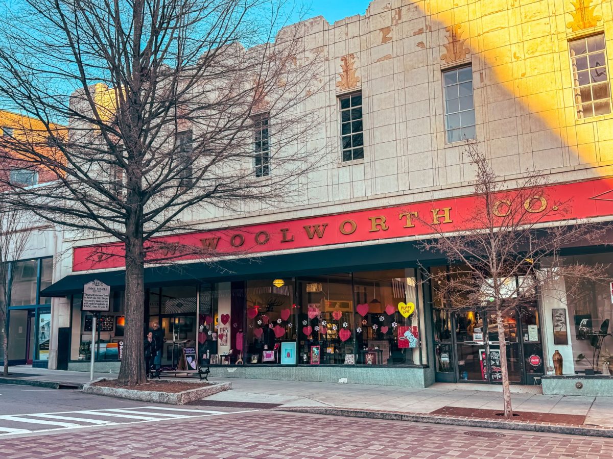 Exterior of the historic Woolworth building in downtown Asheville, NC, with its classic red “Woolworth Co.” signage above large storefront windows along a tree-lined city street.