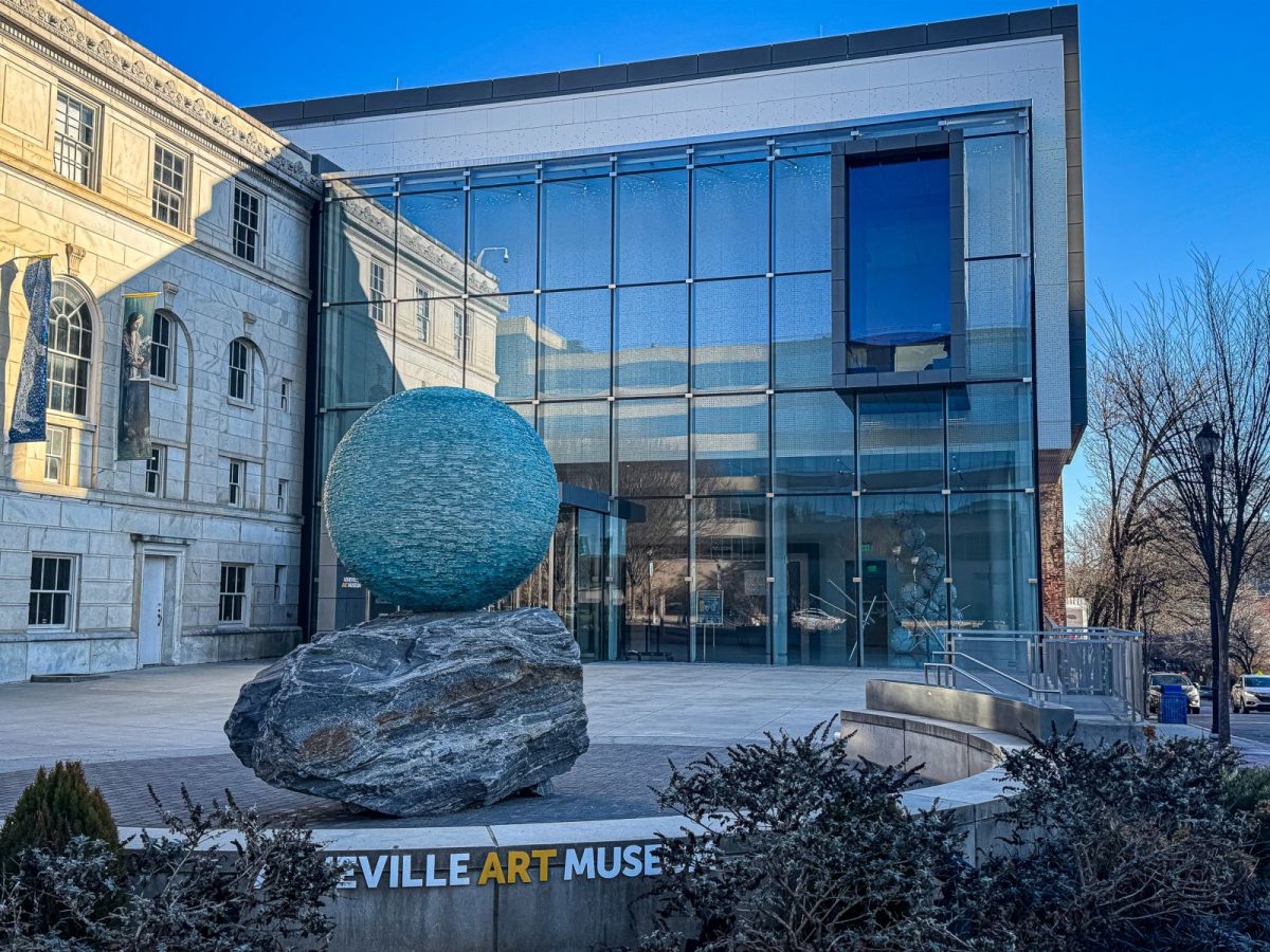 Exterior of the Asheville Art Museum in downtown Asheville, NC, featuring the modern glass façade and large spherical sculpture on a stone base outside the entrance.
