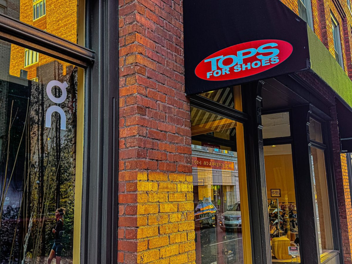 Exterior of Tops For Shoes in downtown Asheville, NC, featuring the red-and-blue storefront sign above the entrance and brick façade along a city sidewalk.