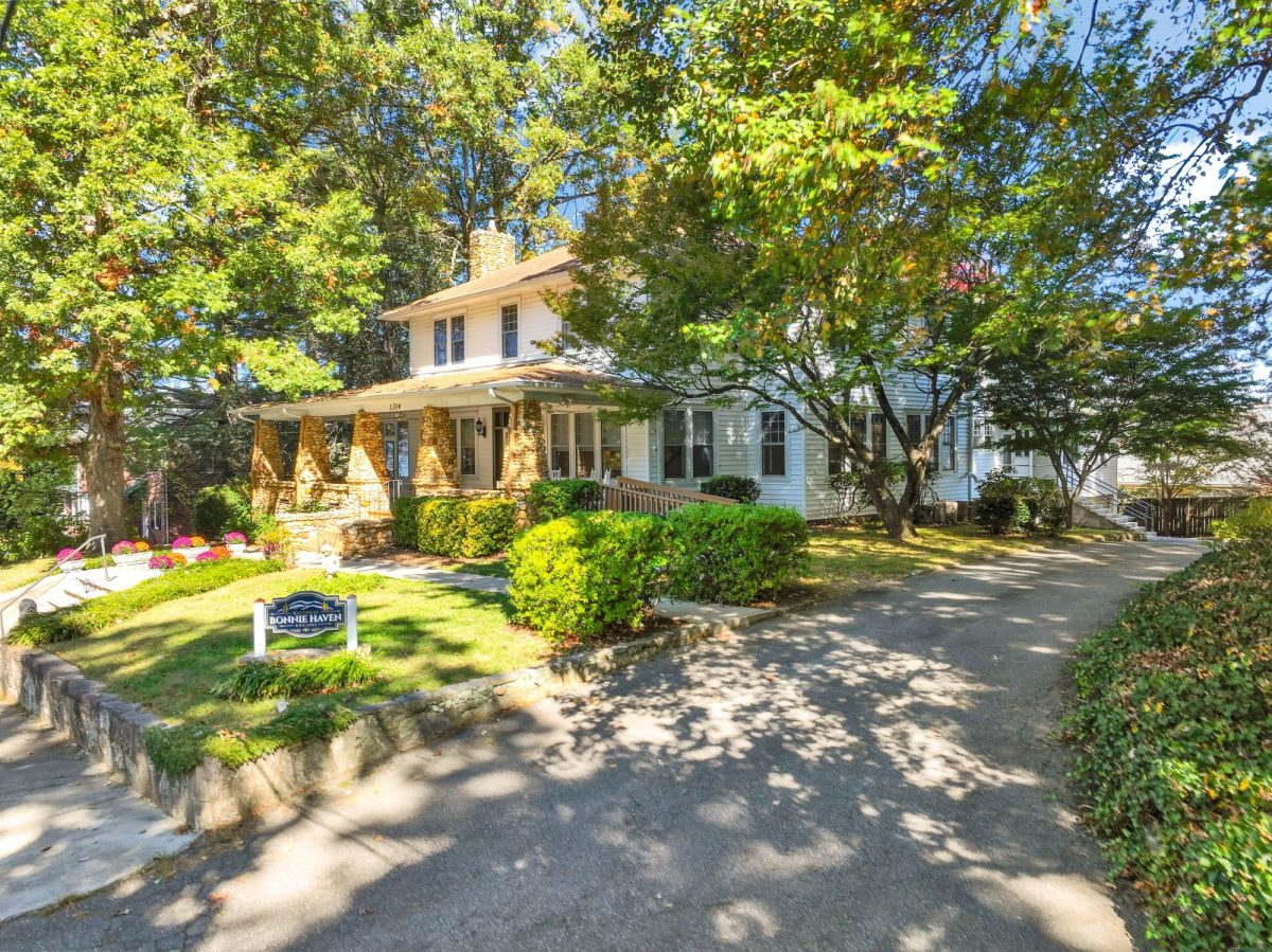 Historic Bonnie Haven vacation rental in Asheville, North Carolina, featuring a classic white mountain home with a stone porch, mature trees, and landscaped grounds.