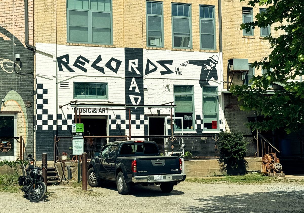 Exterior view of Records in the RAD in Asheville’s River Arts District, featuring bold black-and-white mural-style lettering on a historic brick building with parked vehicles and industrial arts district surroundings.