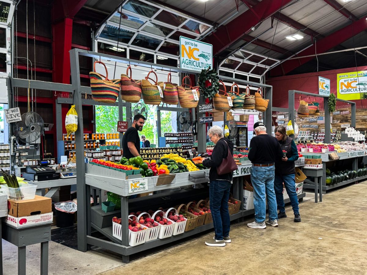 Shoppers browse colorful fresh produce and locally made goods inside the WNC Farmers Market in Asheville, NC, surrounded by baskets, peppers, peaches, and mountain-grown vegetables.
