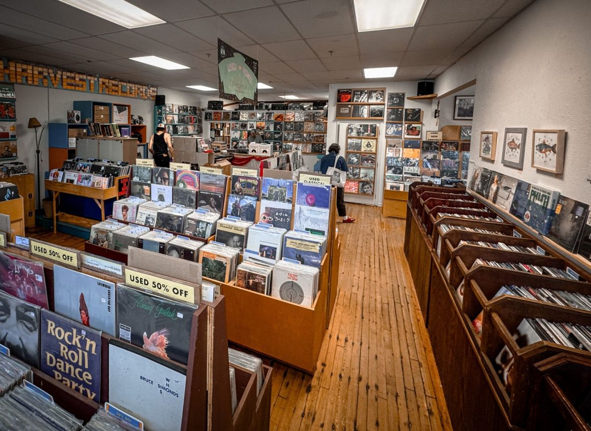 Wide interior view of Harvest Records in West Asheville featuring rows of vinyl records, wooden floors, music lovers browsing albums, and walls lined with new and used records.