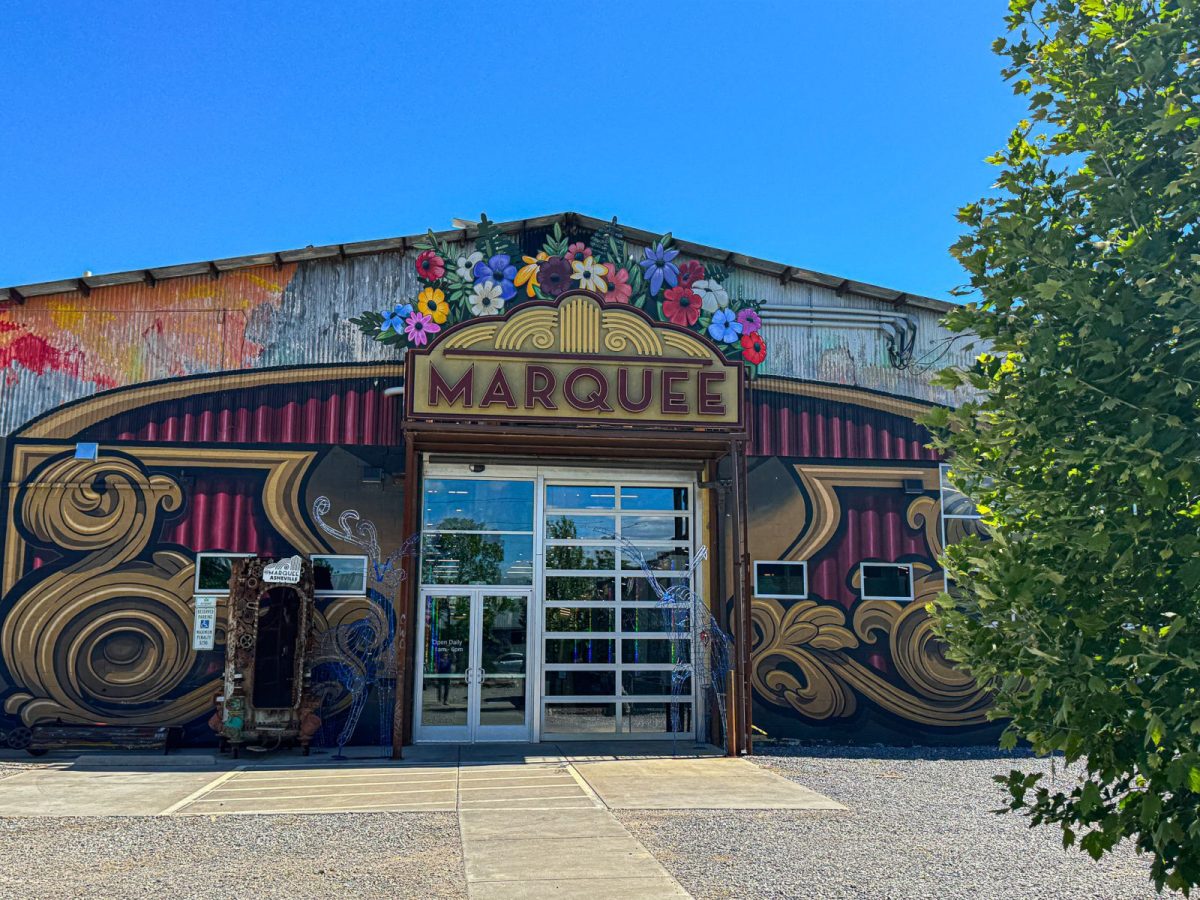 Exterior entrance of The Marquee in Asheville’s River Arts District featuring colorful mural artwork, ornate signage, and the eclectic vintage marketplace facade under a bright blue sky.