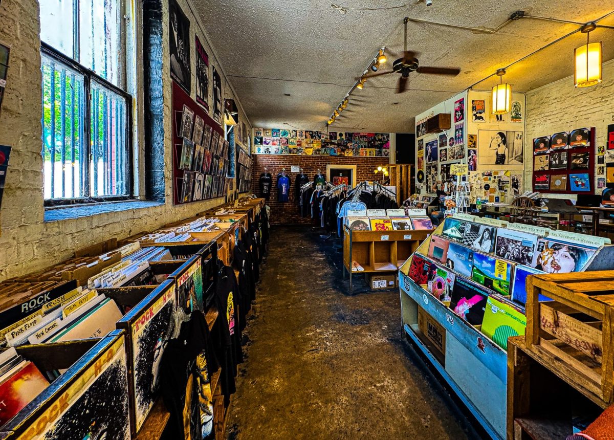 Interior of Voltage Records in downtown Asheville featuring rows of vinyl records, band merchandise, music posters, exposed brick walls, and an eclectic independent record store atmosphere.
