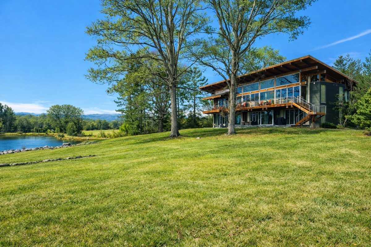 Modern luxury mountain home in Western North Carolina overlooking a peaceful pond and Blue Ridge Mountain views beneath a clear blue sky.