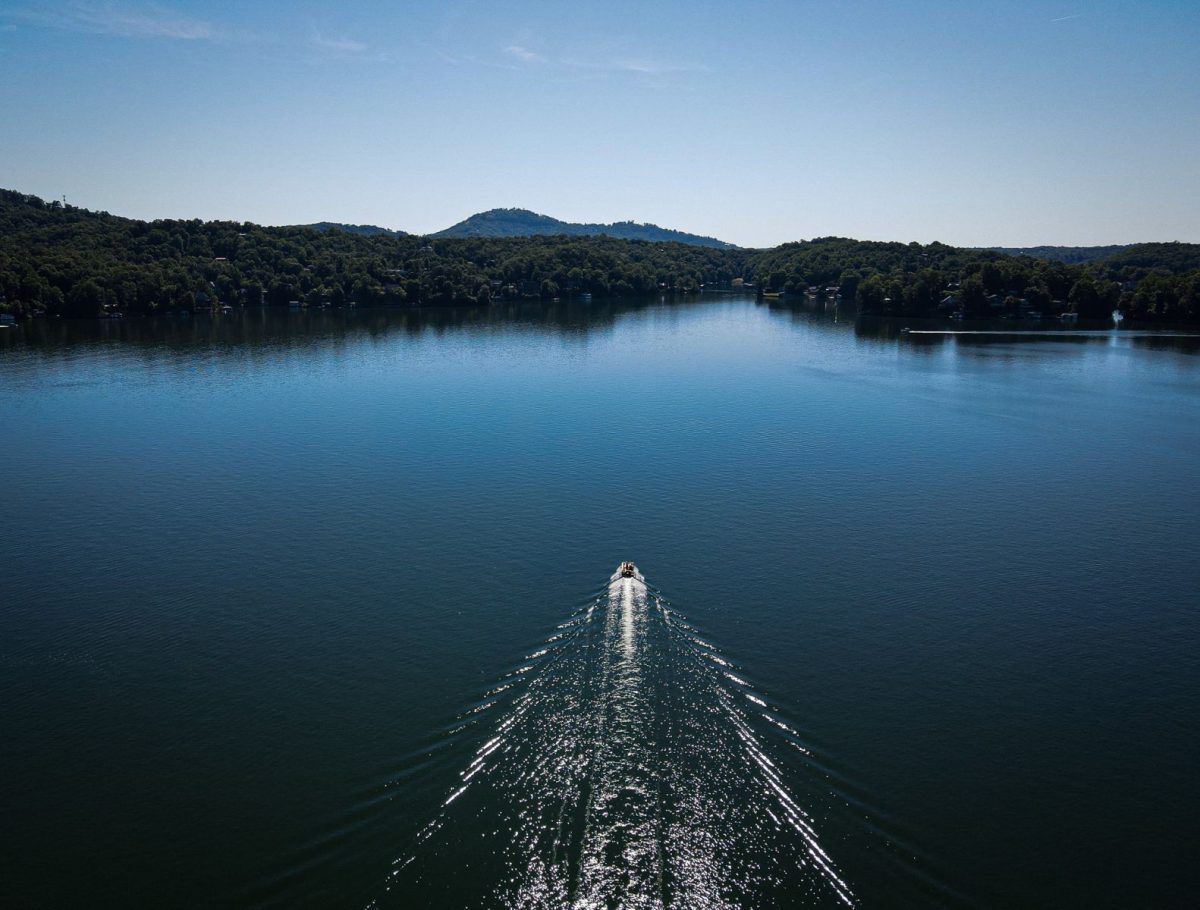 Aerial view of Lake Lure with a boat gliding across calm water, leaving a shimmering wake as forested mountains and lakeside homes stretch across the horizon