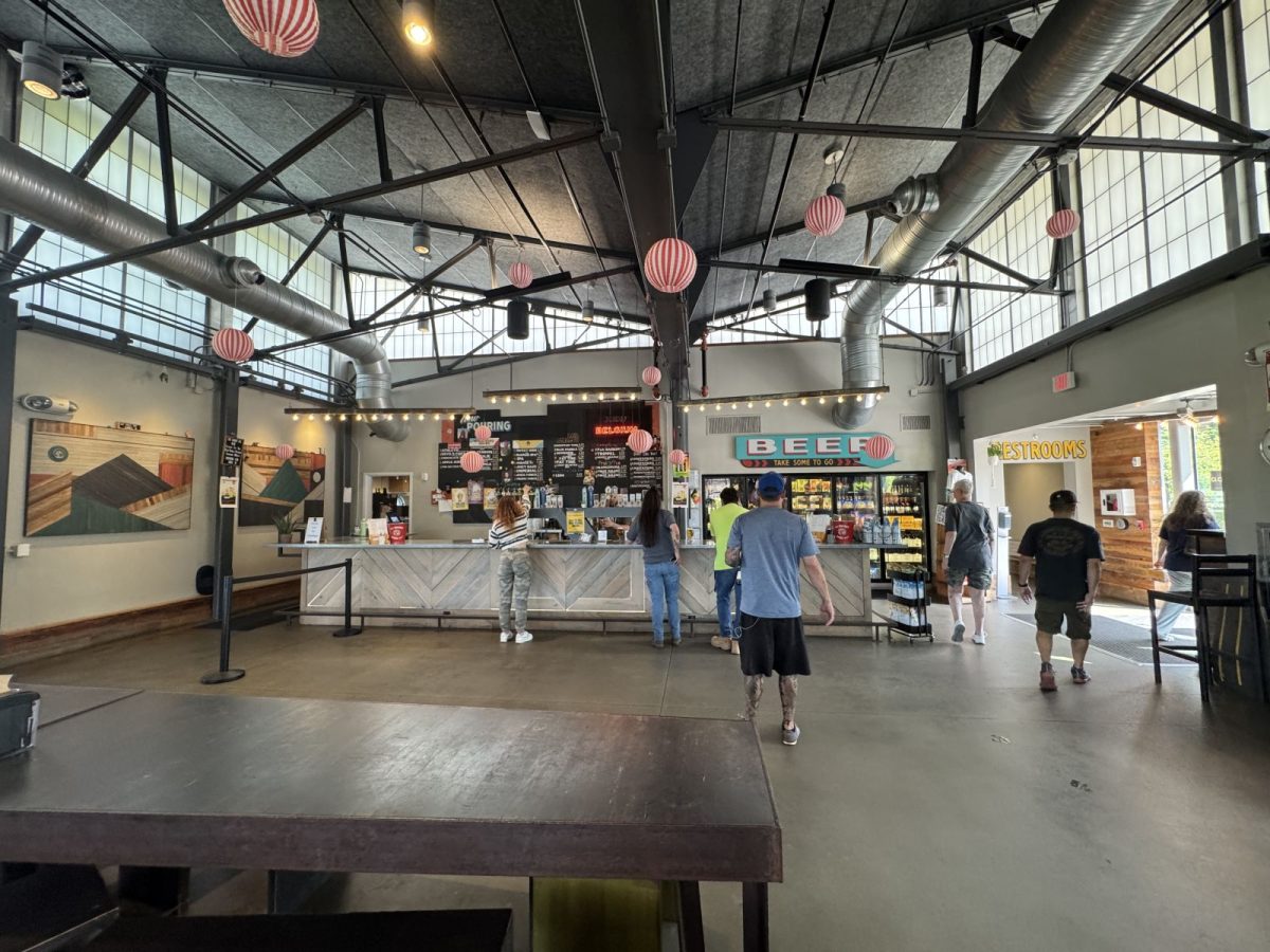 Guests ordering craft beer inside New Belgium Brewing's spacious taproom in Asheville, featuring an industrial-style interior, high ceilings, colorful décor, and a large beer-to-go counter.
