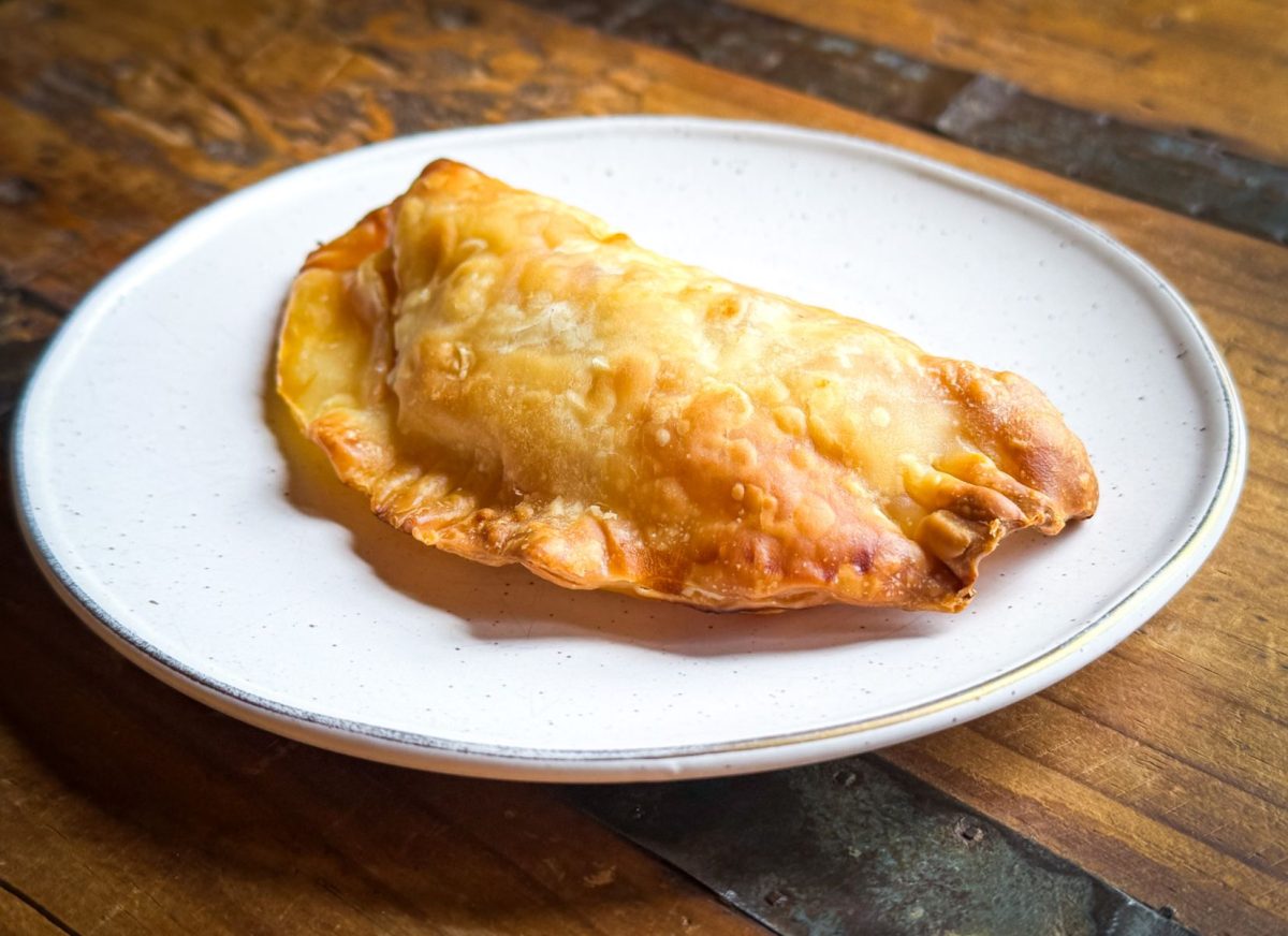 Freshly baked Argentinian-style empanada from Cecilia's Kitchen in Asheville, NC, served on a white plate. The golden, flaky pastry is one of the food truck's most popular menu items.