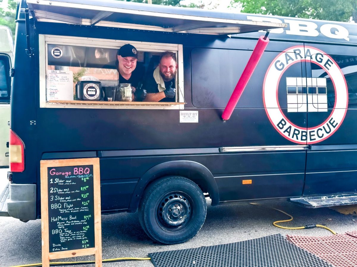 Garage Barbecue food truck in Asheville, NC, serving smoked barbecue specialties from a custom mobile kitchen. Team members greet guests from the service window at a local food truck event.
