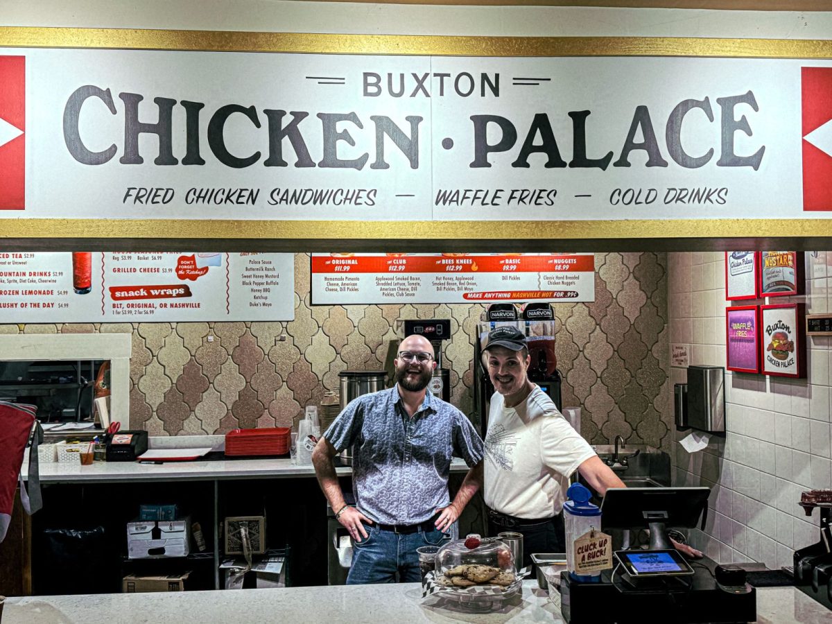 Team members behind the counter at Buxton Chicken Palace in downtown Asheville, North Carolina, beneath the restaurant's signature sign advertising fried chicken sandwiches and waffle fries.