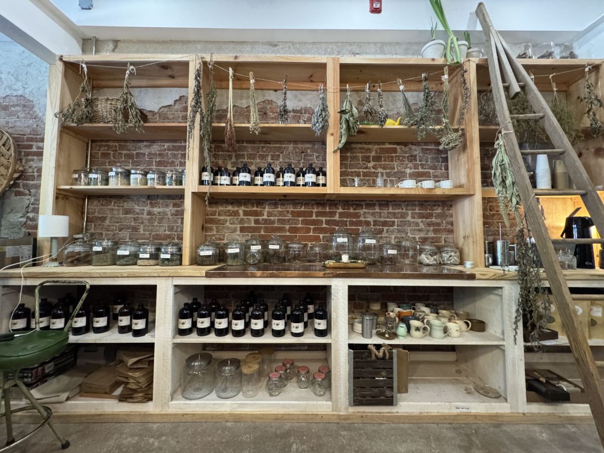 A rustic tea preparation area inside Ginny Lou's in downtown Marshall, North Carolina, featuring dried herbs hanging from wooden shelves, glass jars of loose-leaf teas, handcrafted mugs, and vintage brick walls that create a warm, old-world atmosphere.