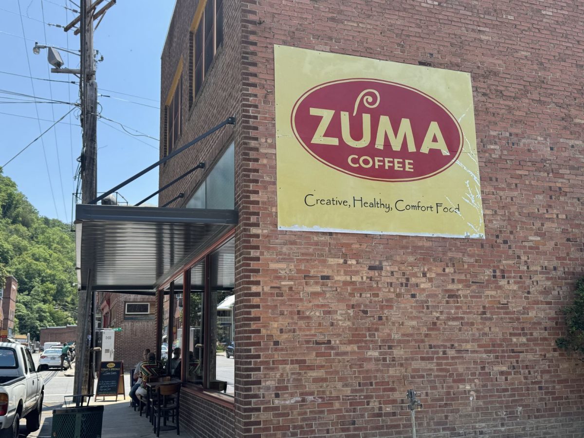 The exterior of Zuma Coffee in downtown Marshall, North Carolina, featuring the restaurant's iconic vintage sign on a red brick building with sidewalk seating and the surrounding mountain town streetscape.