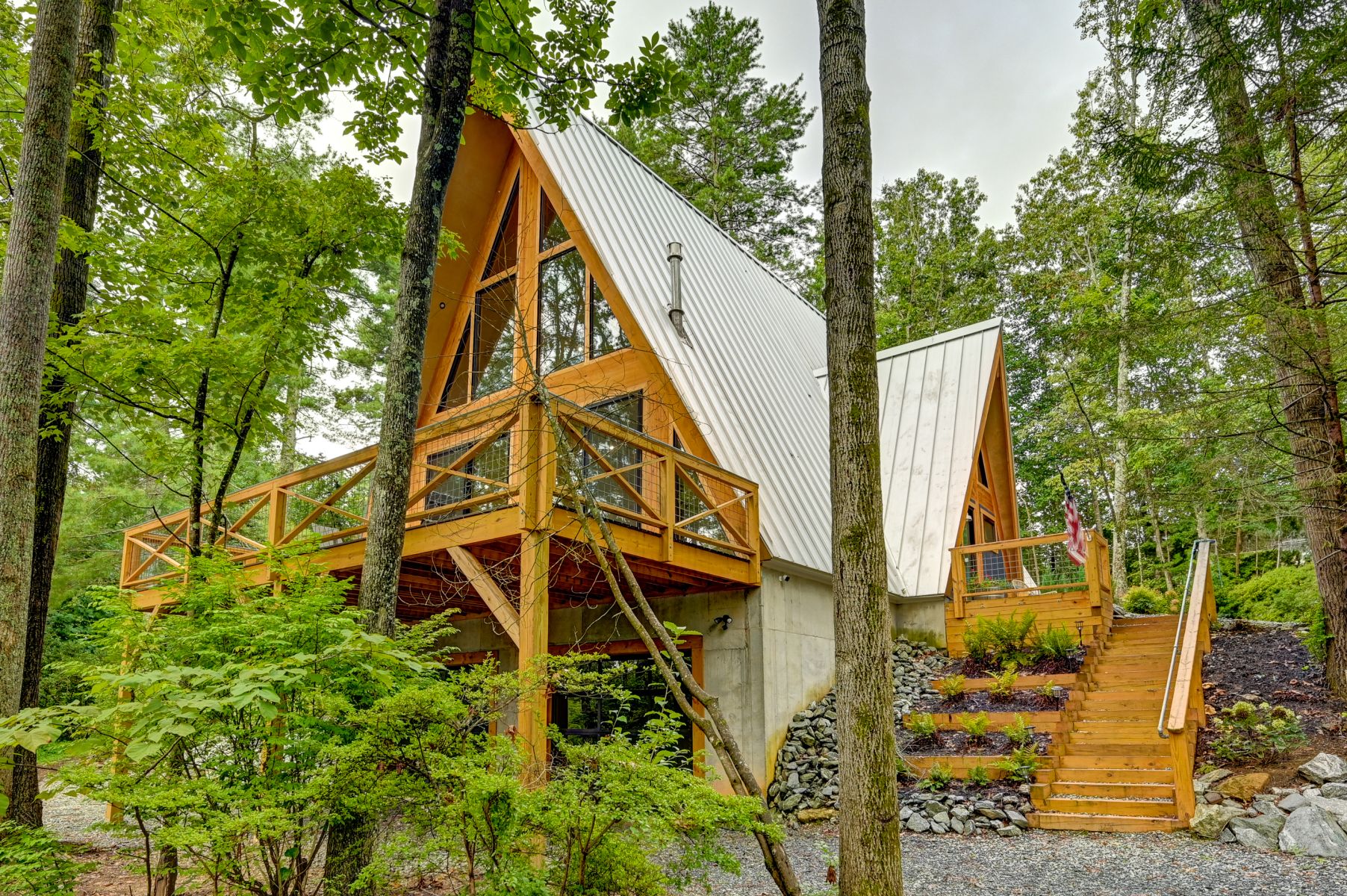 Exterior view of A-Frame Nest, a modern A-frame cabin in Asheville surrounded by lush forest, featuring expansive windows, wraparound decks, a metal roof, and beautifully landscaped mountain grounds.