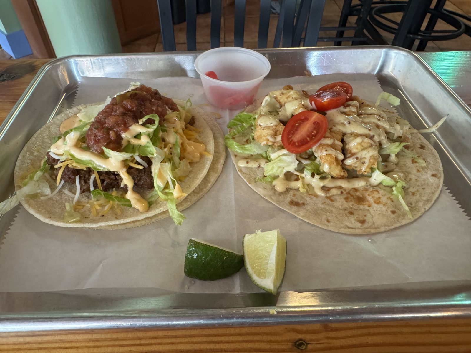 Two tacos from Star Taco in Marshall, NC, served on a metal tray with lime wedges and house-made pickled vegetables. One taco features shredded chicken topped with roasted green salsa and fresh pico de gallo, while the other is a vegetarian taco with black beans, cheese, salsa, and crisp cabbage slaw.