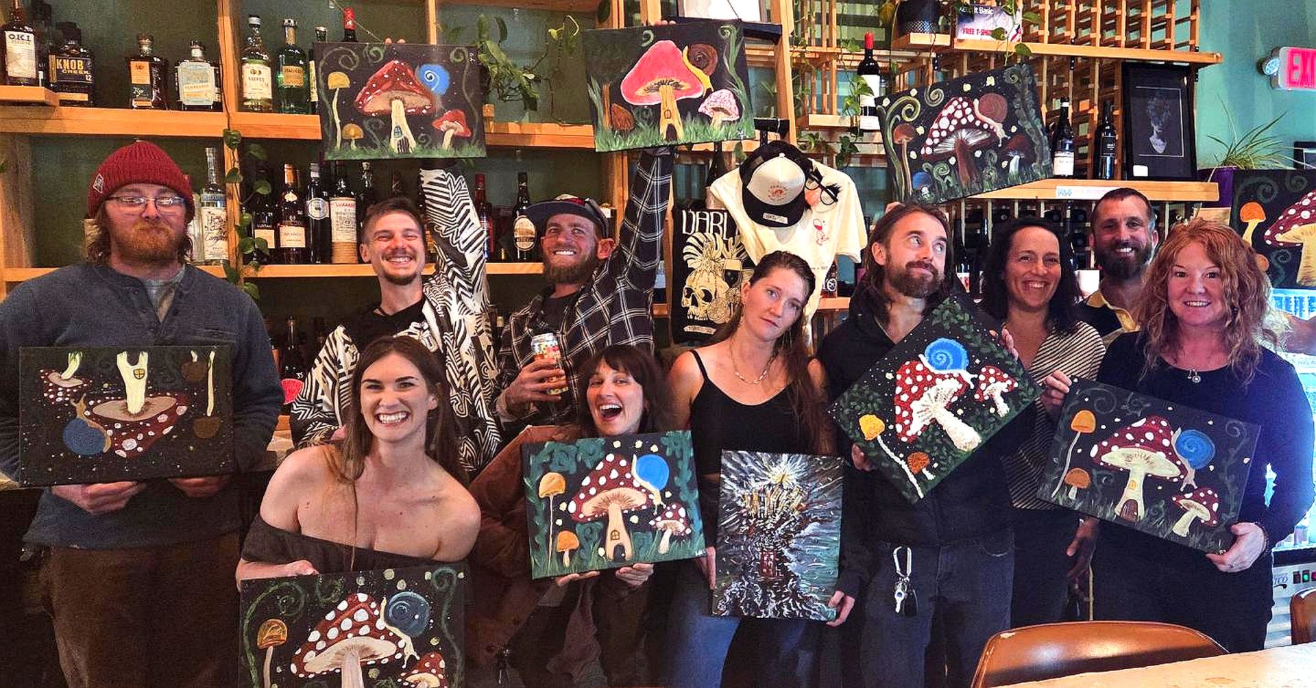 Group of eleven people in a cozy studio, each holding a colorful mushroom painting.