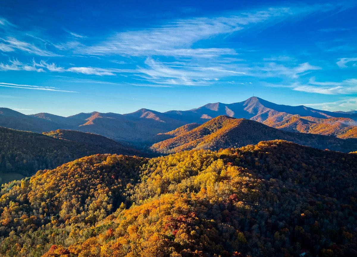 Panoramic view of the Blue Ridge Mountains near Asheville covered in brilliant golden, orange, and red fall foliage beneath a vivid blue autumn sky.