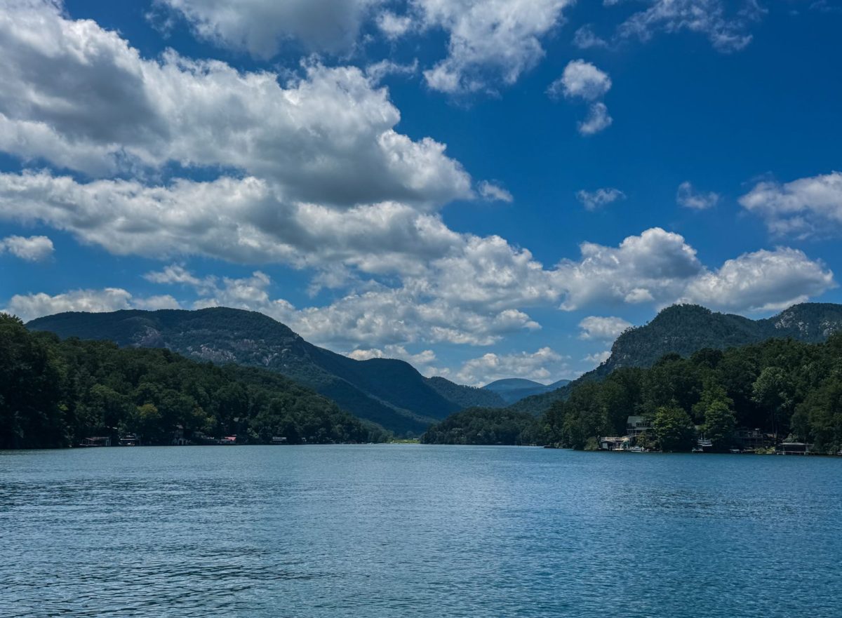 Scenic view of Lake Lure surrounded by the Blue Ridge Mountains under a brilliant blue sky filled with dramatic white clouds in Western North Carolina.
