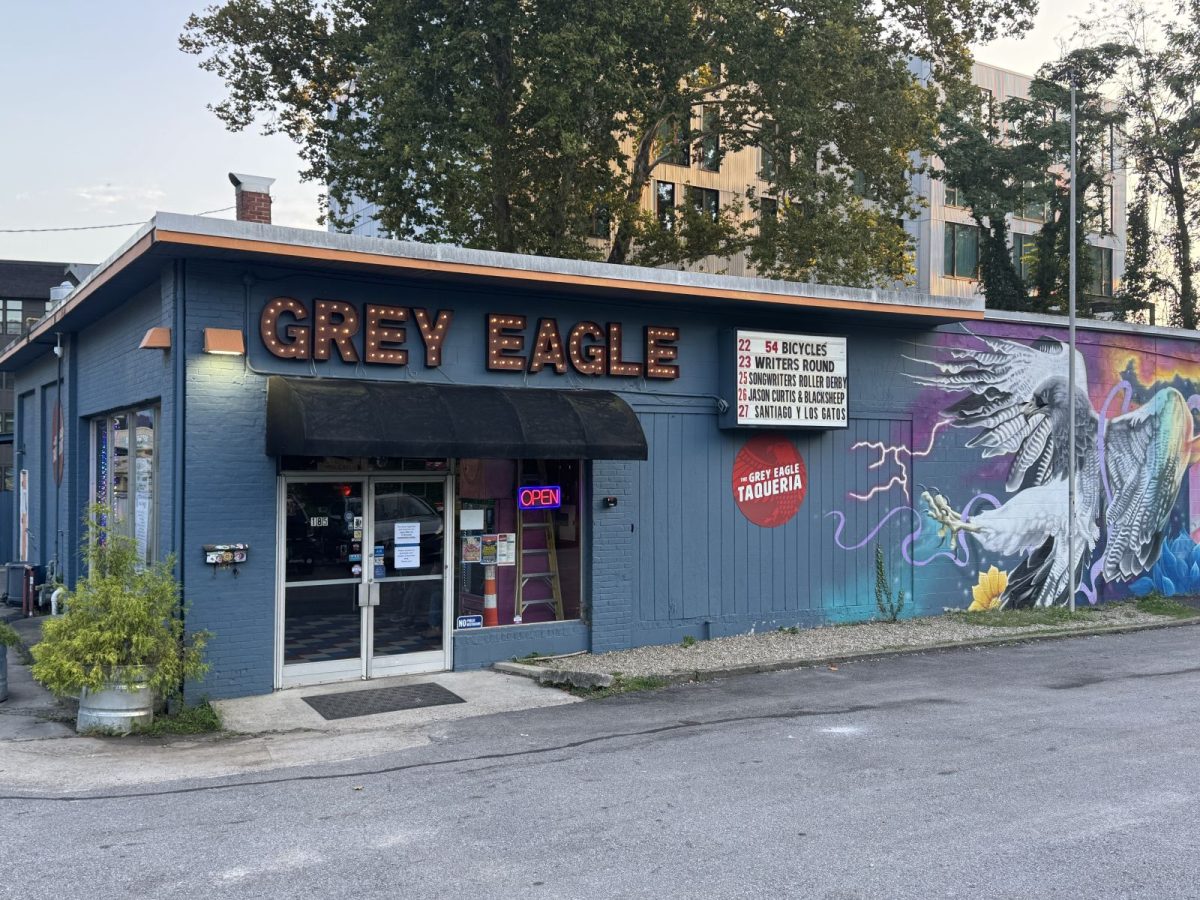 Exterior of The Grey Eagle music venue in Asheville, featuring its illuminated marquee, colorful bird mural, and welcoming entrance on a quiet evening. The venue's iconic signage and adjacent Grey Eagle Taqueria highlight one of the city's most beloved live music destinations.
