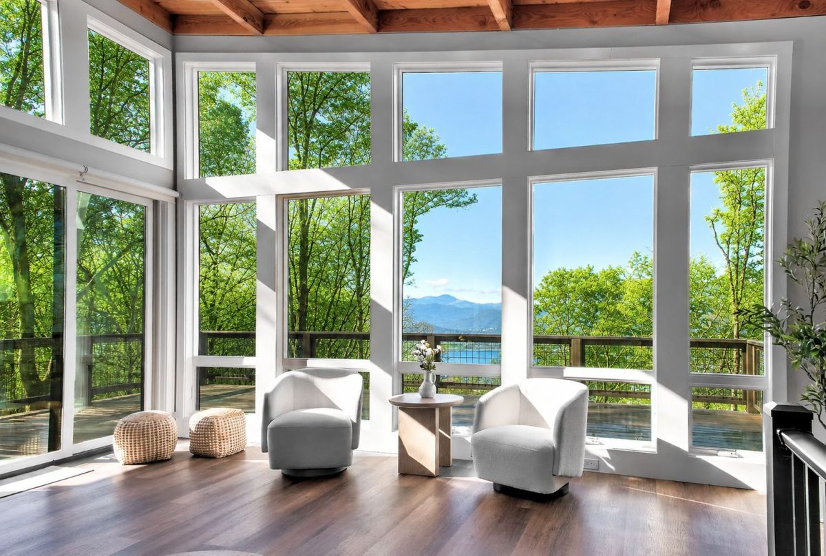 Bright living room at Skyline Ridge with floor-to-ceiling windows, modern seating, vaulted wood-beam ceilings, and panoramic mountain views overlooking Lake Lure.