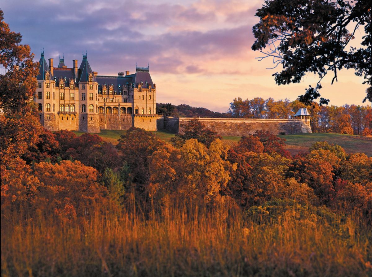 Biltmore Estate in Asheville, North Carolina, surrounded by brilliant orange, red, and golden fall foliage beneath a colorful autumn sunset.