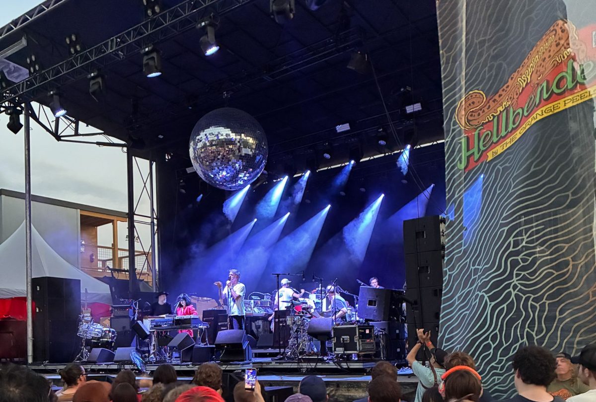 Live band performing under blue stage lights at the Hellbender concert and event stage in Asheville, with a large disco ball overhead and festivalgoers gathered in front.