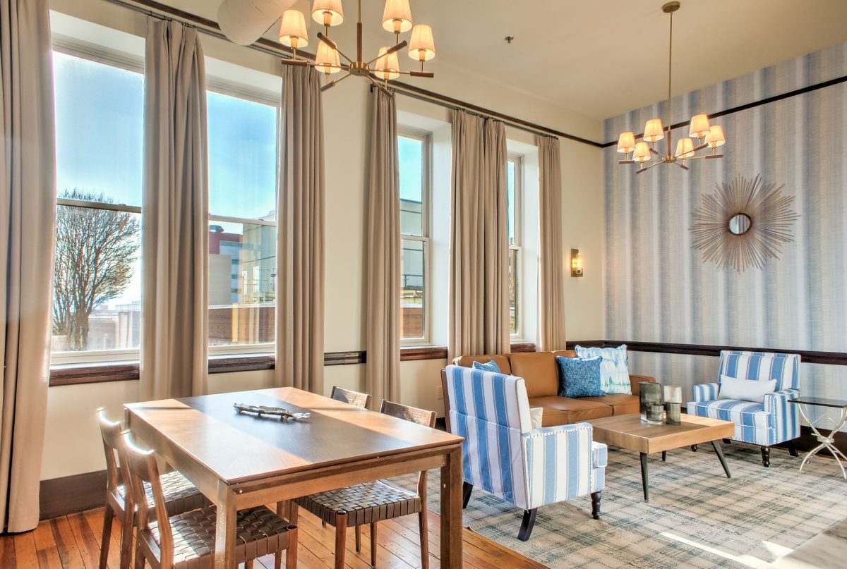 Bright living and dining area inside The Sapphire at The Heirloom in downtown Asheville, featuring tall windows, hardwood floors, blue-accented furnishings, and abundant natural light.