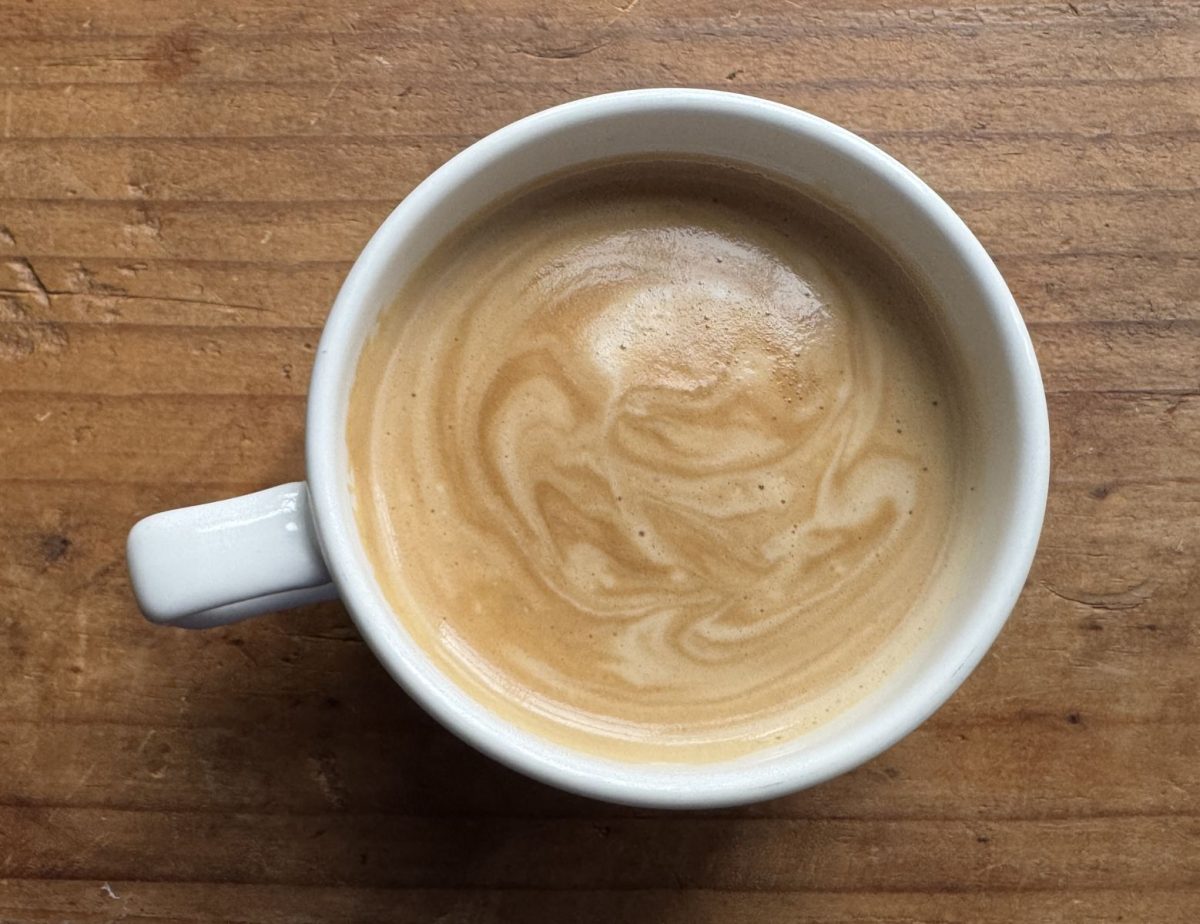 Top-down view of a white mug with latte art swirls in creamy coffee on a wooden table.