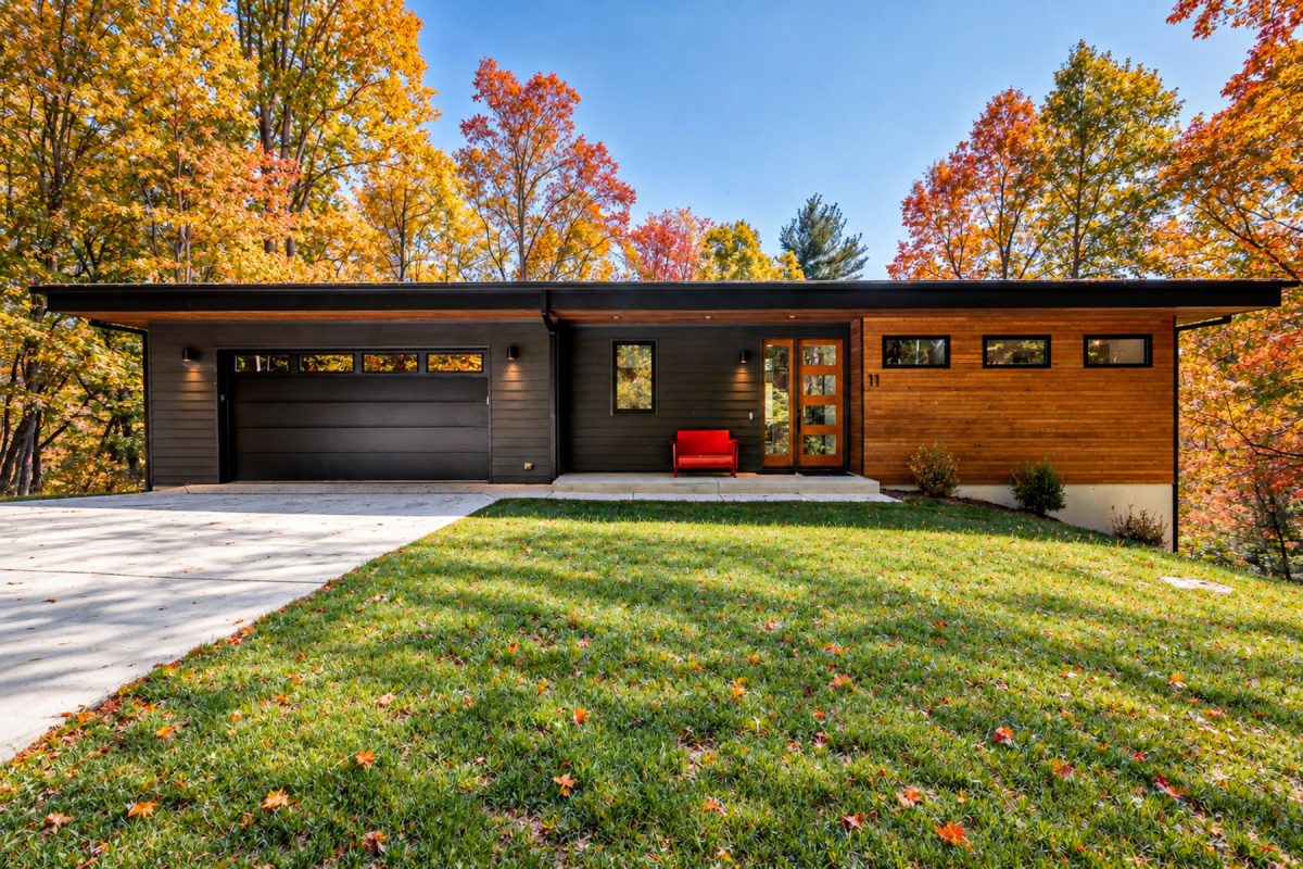 Exterior of Mountain to Sea Modern, a contemporary Asheville vacation home with wood and dark siding, surrounded by vibrant red, orange, and golden fall foliage.