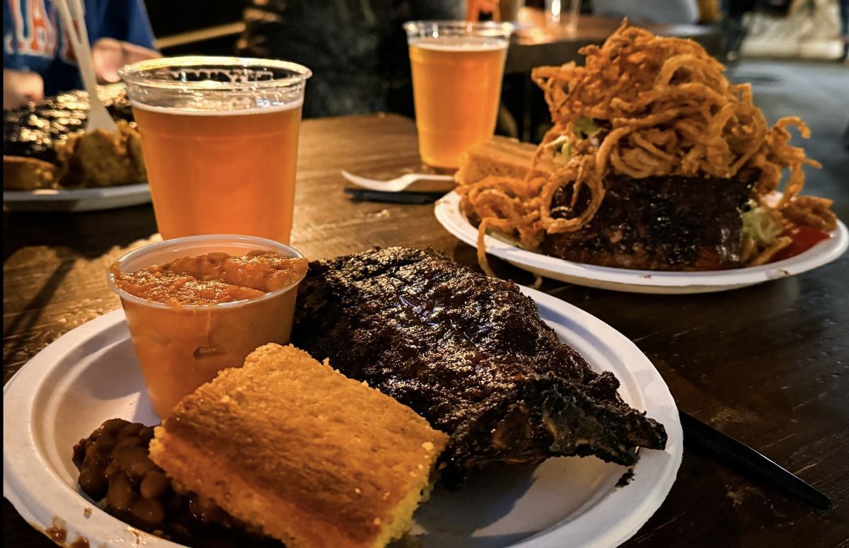 Barbecue ribs with cornbread, baked beans and a side at 12 Bones Smokehouse in Asheville, with another barbecue plate and local craft beers in the background.