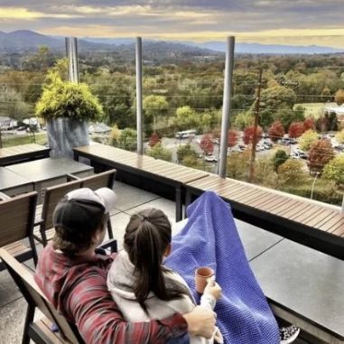 Couple relaxing together on a rooftop patio overlooking colorful fall foliage and the Blue Ridge Mountains near Asheville, North Carolina.