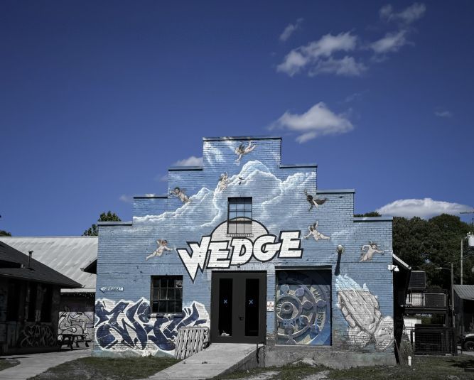 Wedge Brewing building in Asheville’s River Arts District, featuring colorful murals and the distinctive Wedge logo beneath a bright blue sky.