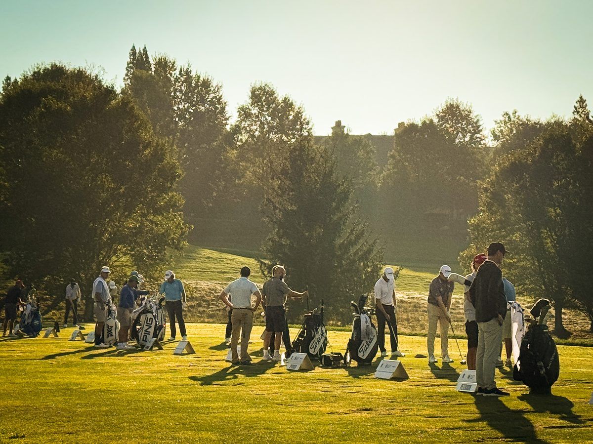 Professional golfers and caddies practice on the driving range at the 2026 Biltmore Championship Asheville at The Cliffs at Walnut Cove, surrounded by trees in the morning sunlight.