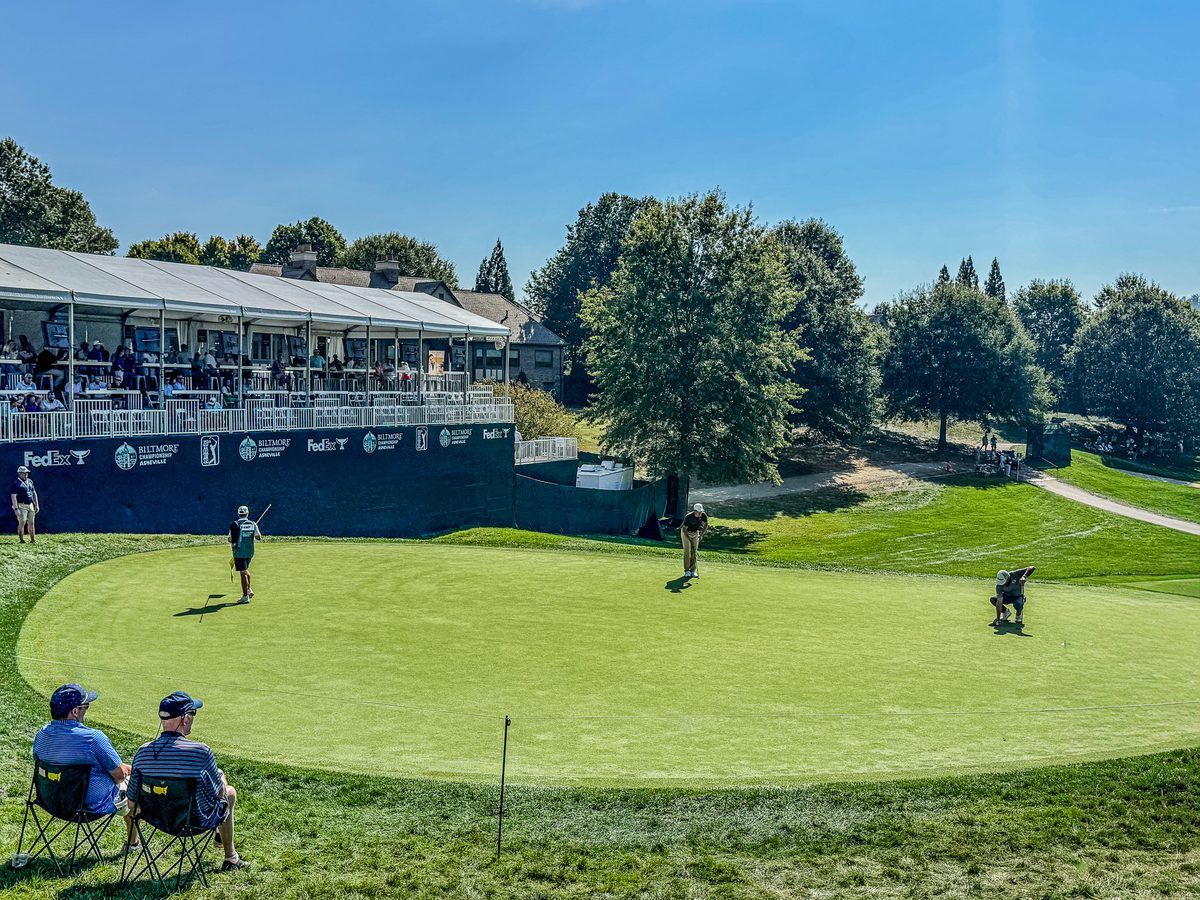 PGA TOUR golfers line up putts on the green at the 2026 Biltmore Championship Asheville at The Cliffs at Walnut Cove, with spectators watching from a nearby hospitality pavilion.