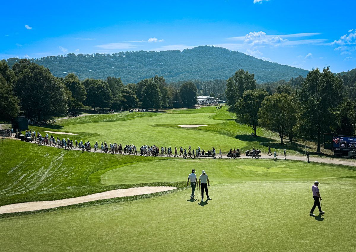 Panoramic view of the 2026 Biltmore Championship Asheville at The Cliffs at Walnut Cove, with PGA TOUR golfers on the green, spectators following the action, and the Blue Ridge Mountains in the background.