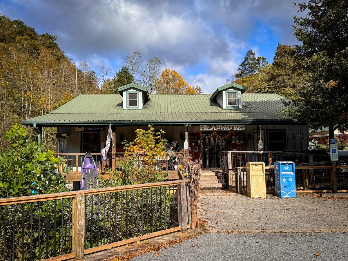 Headwaters Outfitters visitor center in Rosman, North Carolina, featuring a rustic wooden building with a green metal roof, surrounded by colorful autumn foliage in the Blue Ridge Mountains.