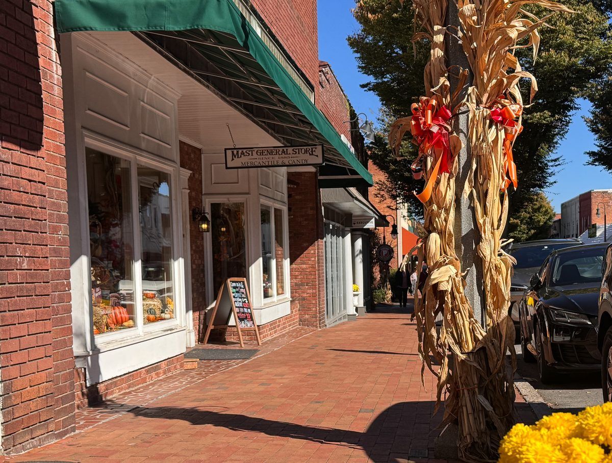 Mast General Store on Main Street in downtown Waynesville, North Carolina, featuring historic brick storefronts, a green awning, and festive fall decorations with pumpkins and cornstalks.