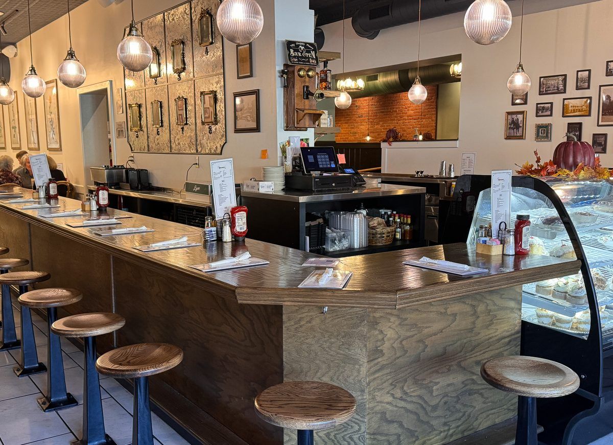 Interior of Main Street Diner in Waynesville, NC, featuring a classic wooden dining counter, bar stools, pendant lighting, vintage décor, and a display case filled with desserts.