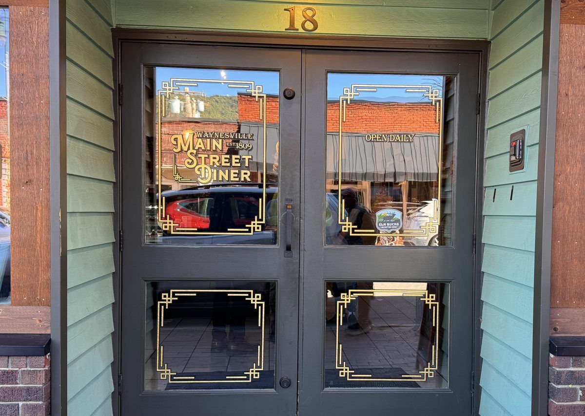 Entrance to Main Street Diner in downtown Waynesville, North Carolina, featuring black double doors with decorative gold lettering and vintage-style details.