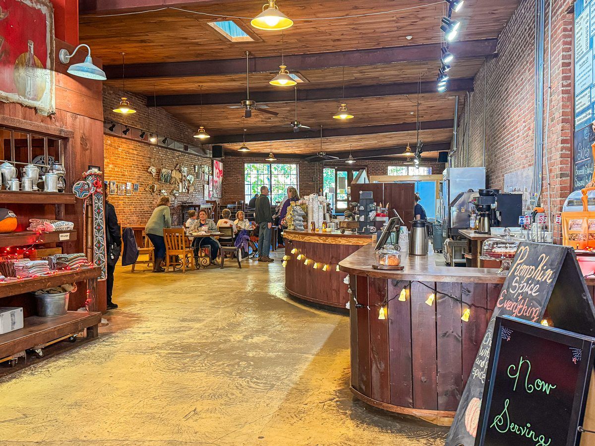 Interior of Panacea Coffee Co. in Waynesville, North Carolina, featuring exposed brick walls, rustic wooden ceilings, a spacious coffee counter, and guests enjoying the welcoming café atmosphere.