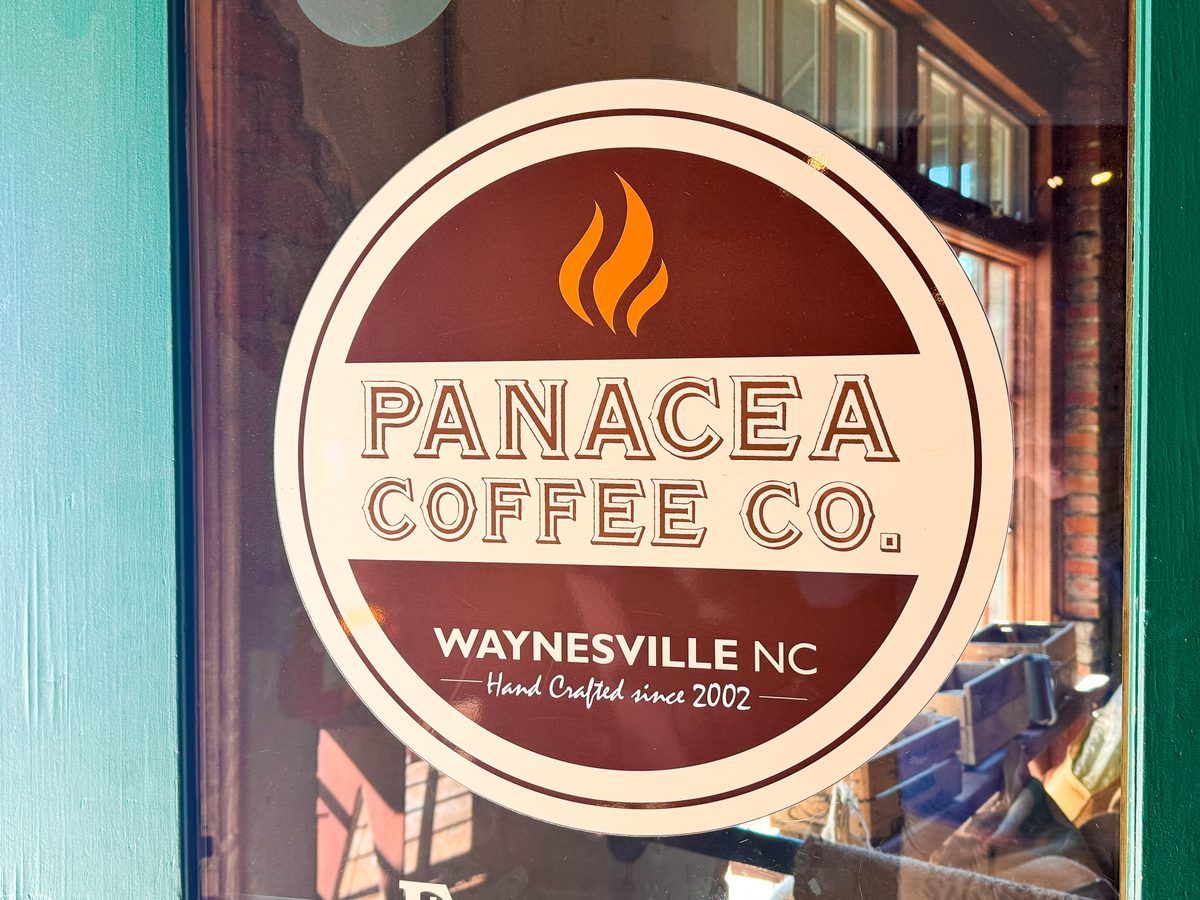 Panacea Coffee Co. logo displayed on the front window of the popular coffee shop in downtown Waynesville, North Carolina, featuring its handcrafted coffee branding established in 2002.